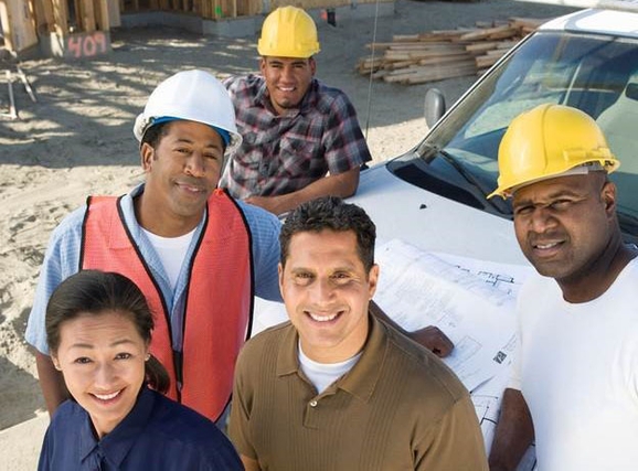 Four men and one woman, standing near a white vehicle on a construction site.